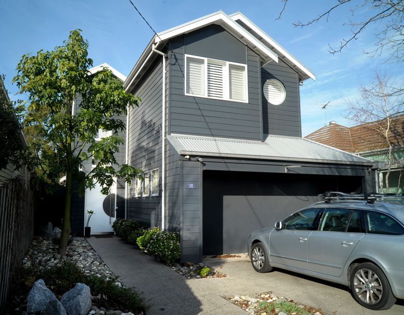 A silver car is parked in front of a grey house
