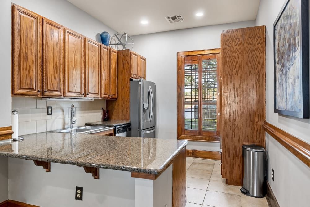 Apartment kitchen with granite counter tops, wooden cabinets, a refrigerator, a sink, and a trash can at Marquis at The RIM in Northwest San Antonio, TX.