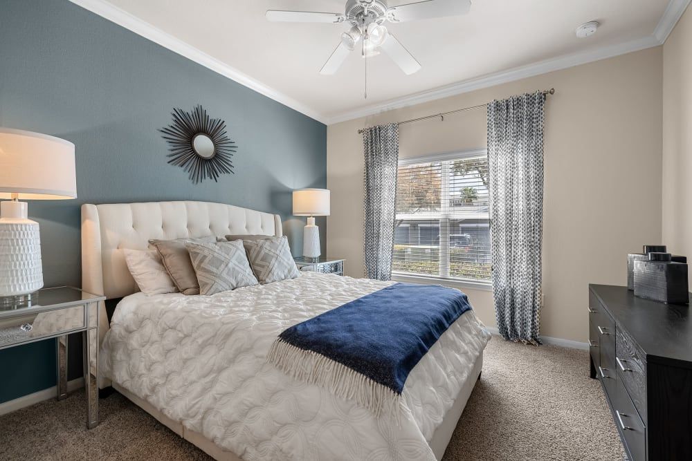 Modern bedroom with a bed, dresser, lamps, and a ceiling fan at Marquis at The RIM in Northwest San Antonio, TX.