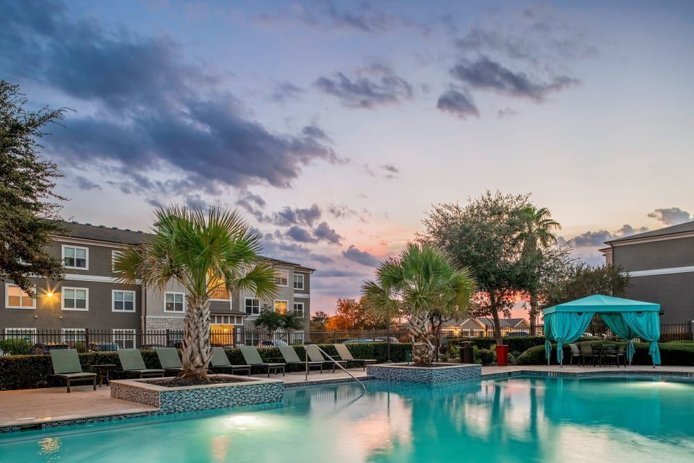 A large swimming pool surrounded by chairs and umbrellas in front of a building at Marquis at The RIM in Northwest San Antonio, TX.