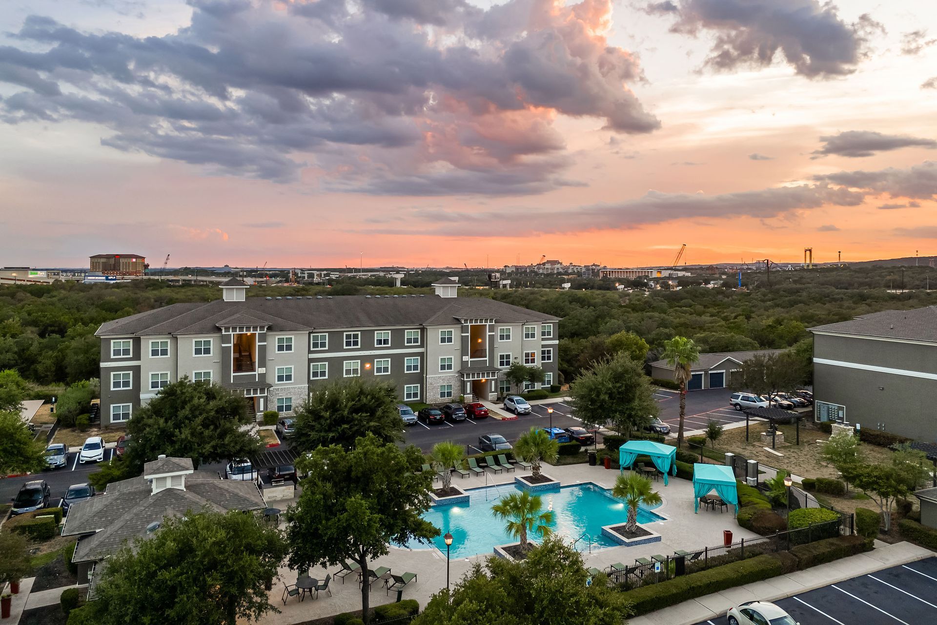 An aerial view of a large apartment complex with a swimming pool at sunset at Marquis at The RIM in Northwest San Antonio, TX.