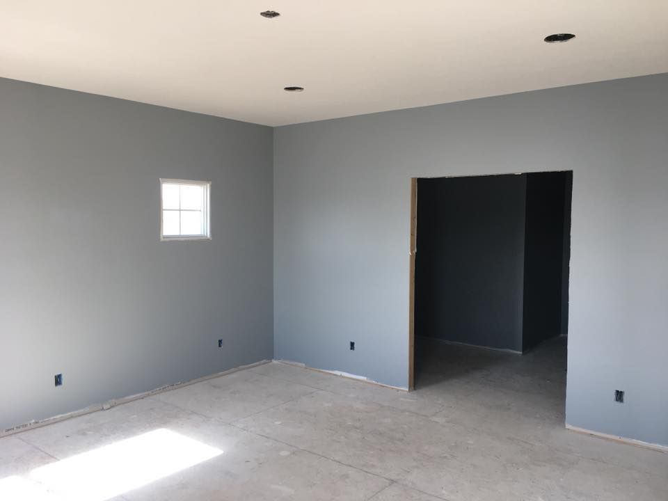 Empty gray room with a small window, recessed lights, and an open doorway to a dark adjoining space