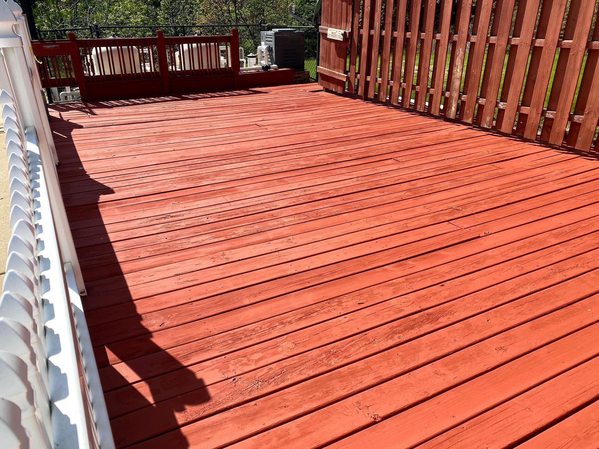 Red wooden deck with railings in bright sunlight, viewed from one end.