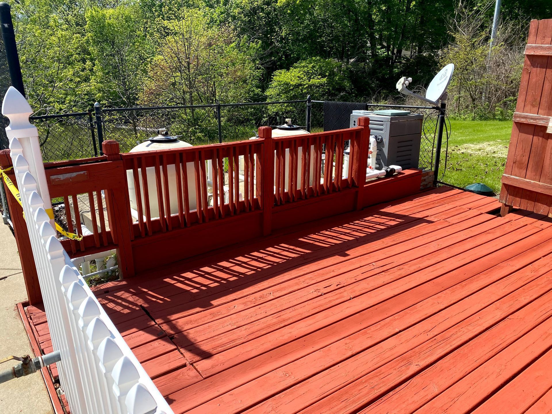 Red wooden deck with railing and stairs overlooking a green backyard