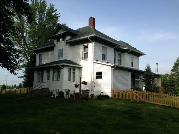 White two-story house with green trim, a garage, and a wooden fence on a grassy yard