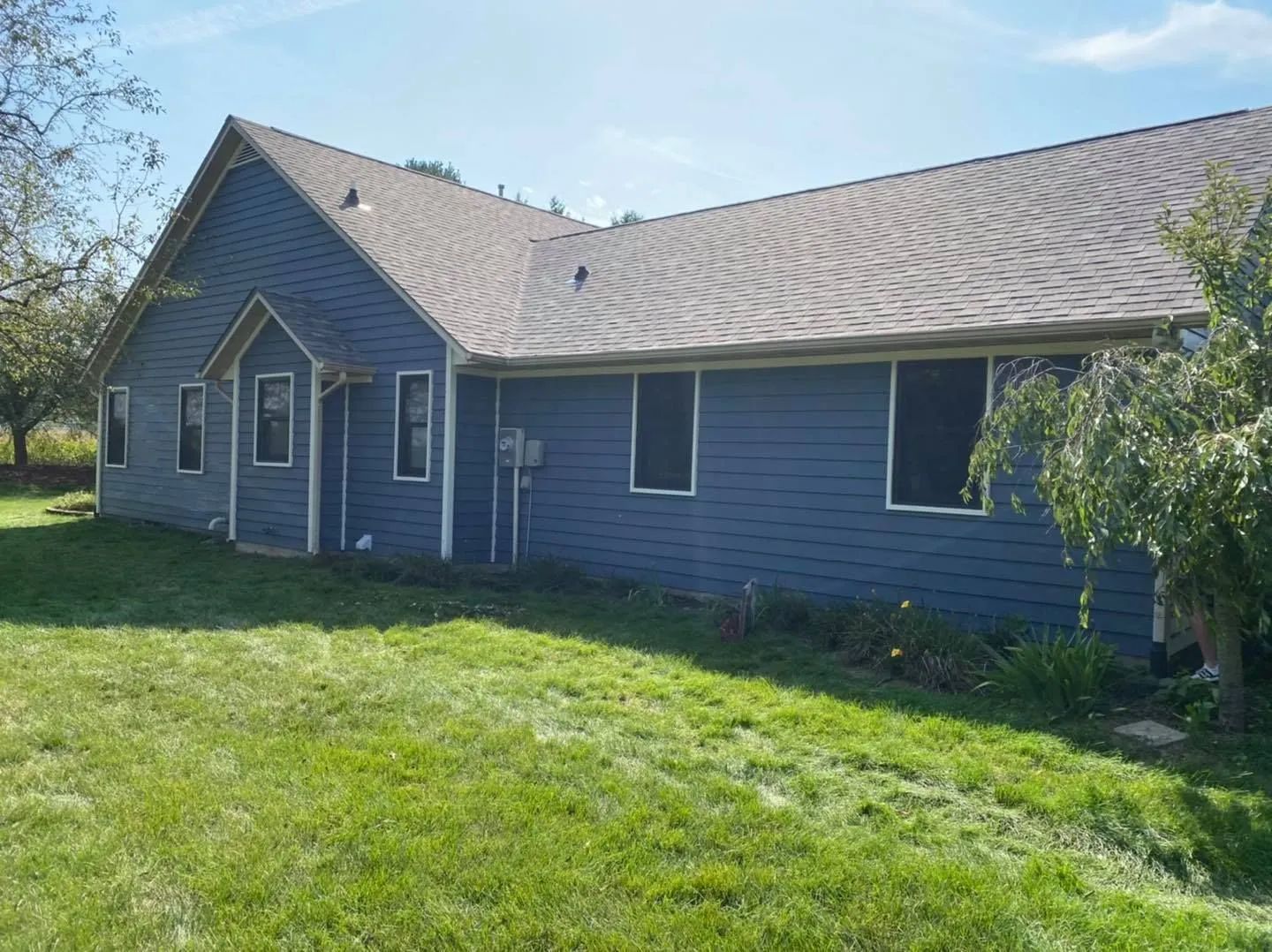 Blue house with a steep roof and grassy lawn under a clear sky