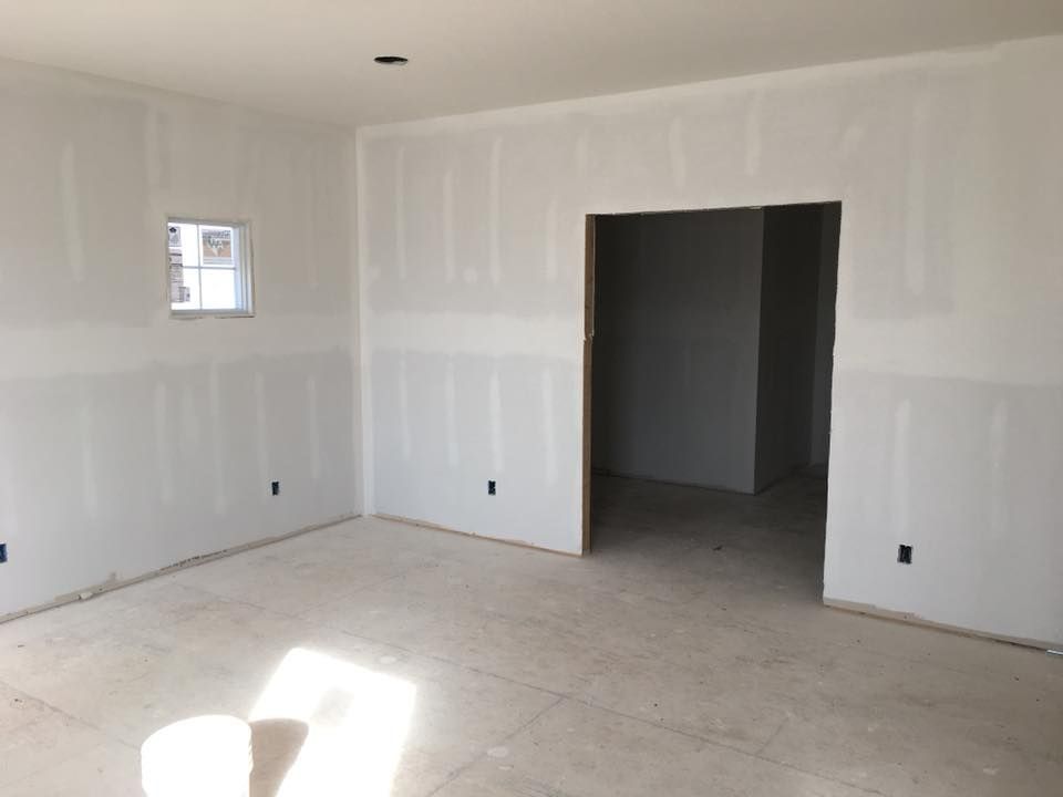Empty unfinished room with white walls, concrete floor, and doorway opening into a dark adjacent space