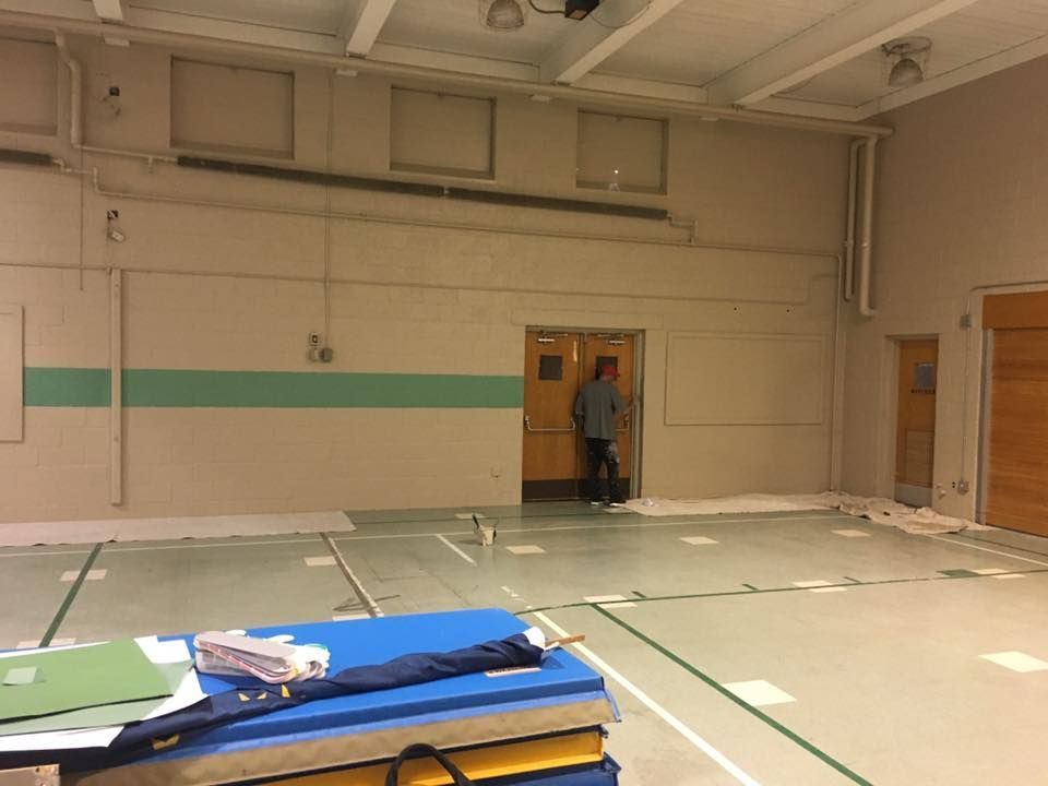 Empty gymnasium with a person standing in a doorway, blue mats in the foreground.