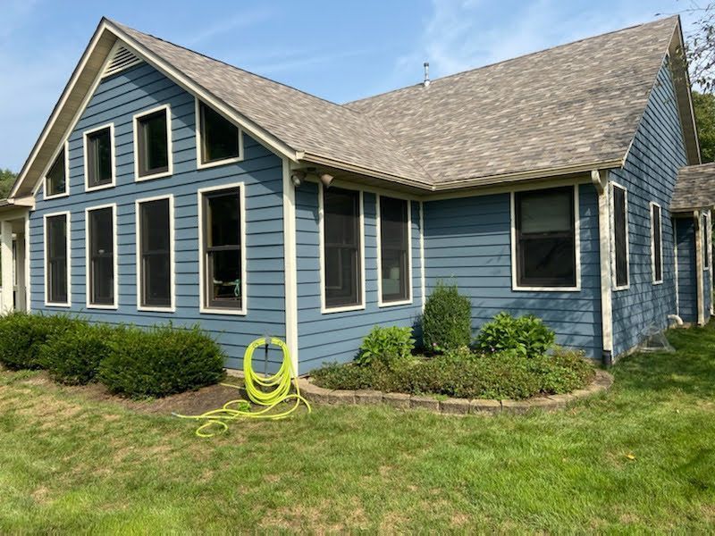 Blue house with white trim, gabled roof, and neatly trimmed shrubs on a sunny lawn