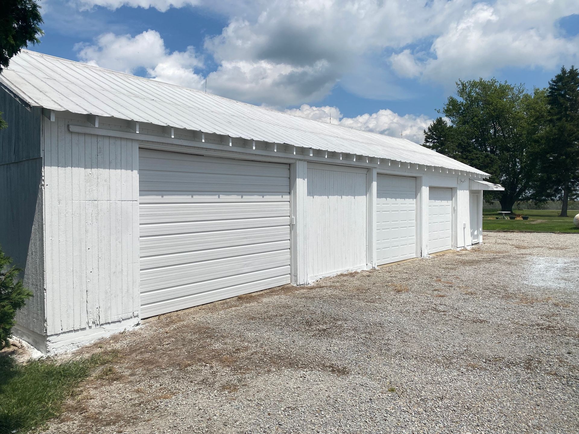 White garage building with multiple doors beside a gravel lot under a partly cloudy sky