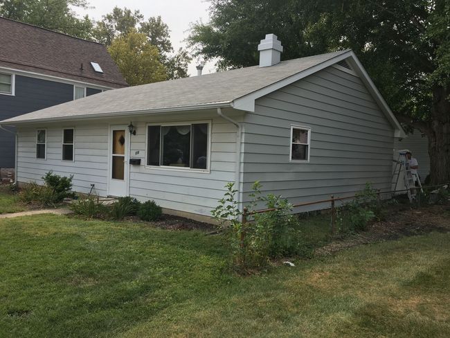 Small gray single-story house with a front porch, white trim, and a grassy yard