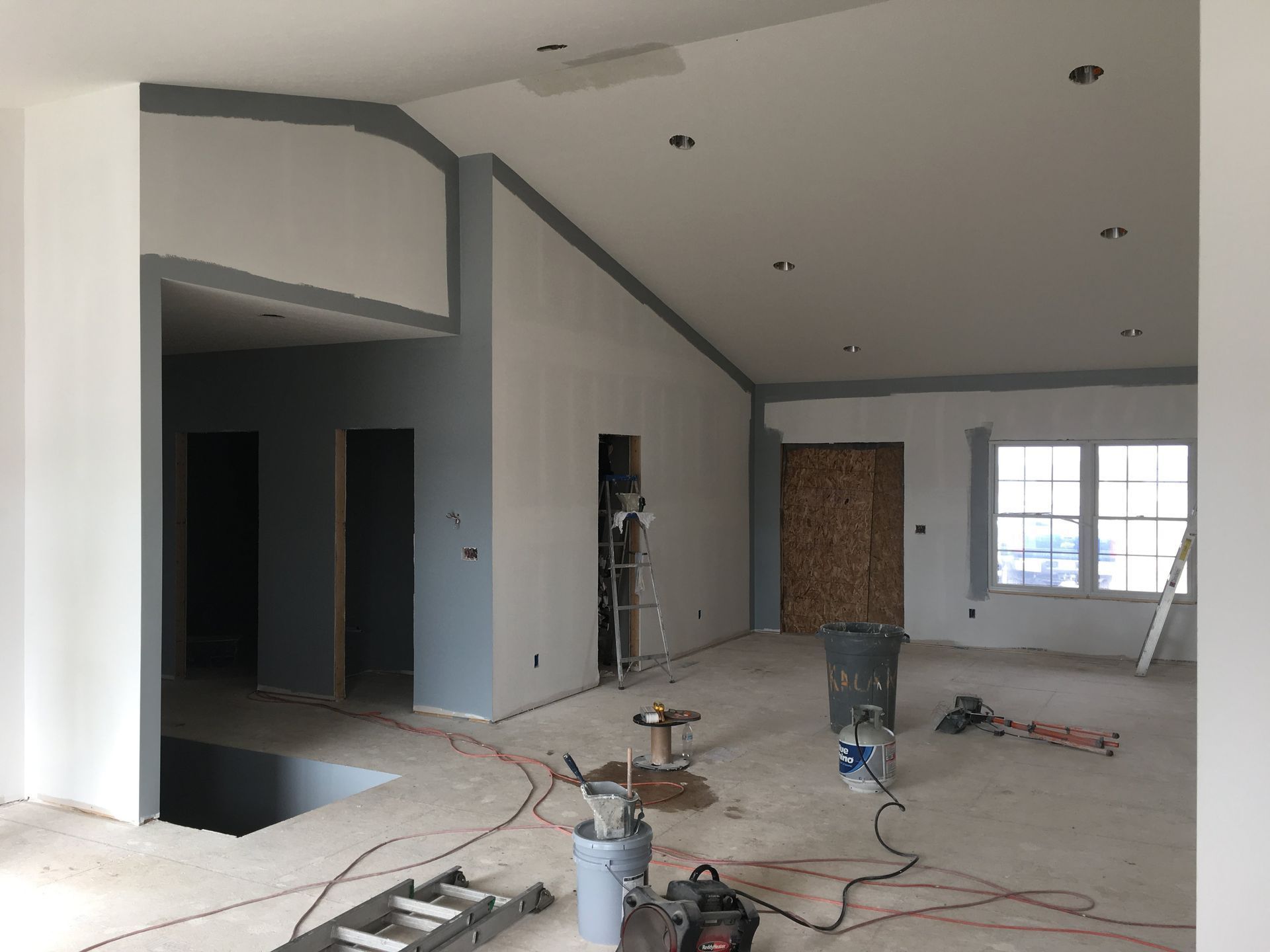 Renovation of a large unfinished room with white walls, exposed flooring, tools, and debris scattered inside