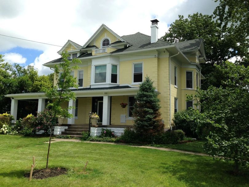 Yellow two-story house with porch and green lawn under a partly cloudy sky
