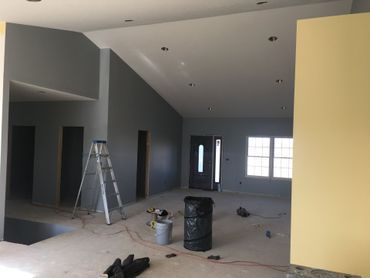 Empty modern room under construction with gray walls, ladder, paint buckets, and a yellow accent wall