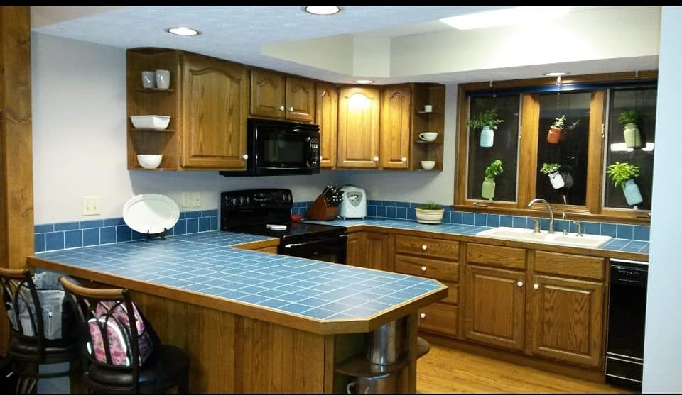 Bright kitchen with blue countertops, wooden cabinets, a sink, stove, and a window over the sink.