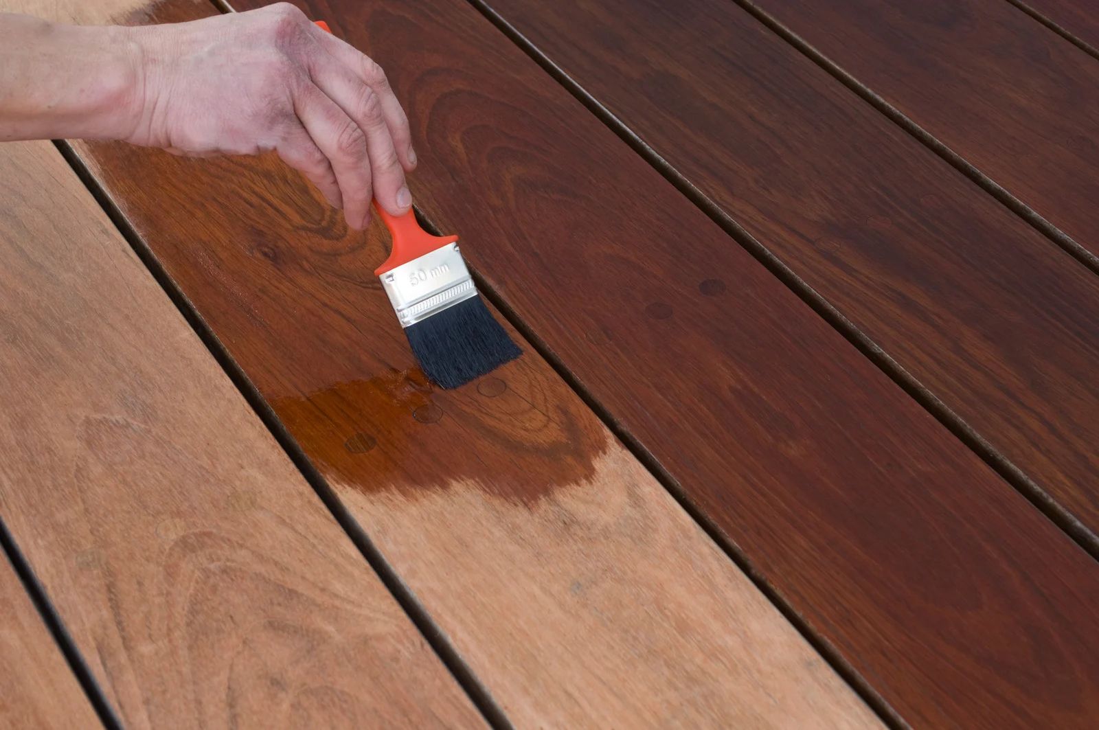 Hand brushing stain onto a wooden deck plank, matching the darker finished boards nearby