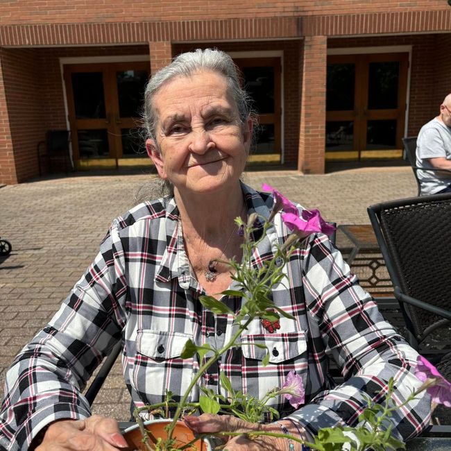 An elderly woman is sitting at a table holding a potted plant.