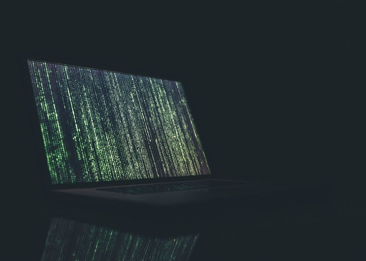 A laptop computer with a green screen is sitting on a table in the dark.