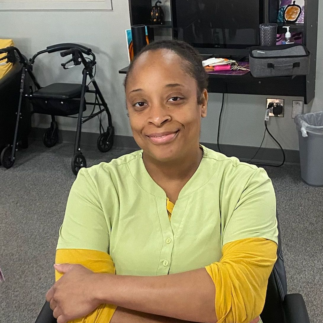 A woman in a green shirt is sitting in a chair with her arms crossed.
