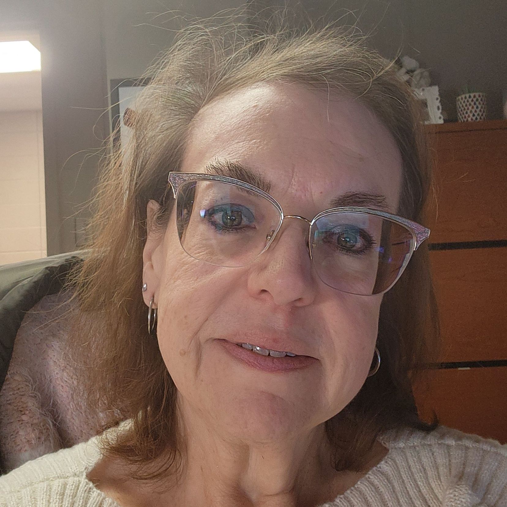 A woman wearing glasses and earrings is smiling for the camera.