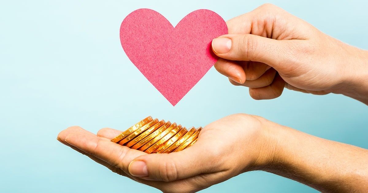 A person is holding a heart and a pile of coins in their hands.