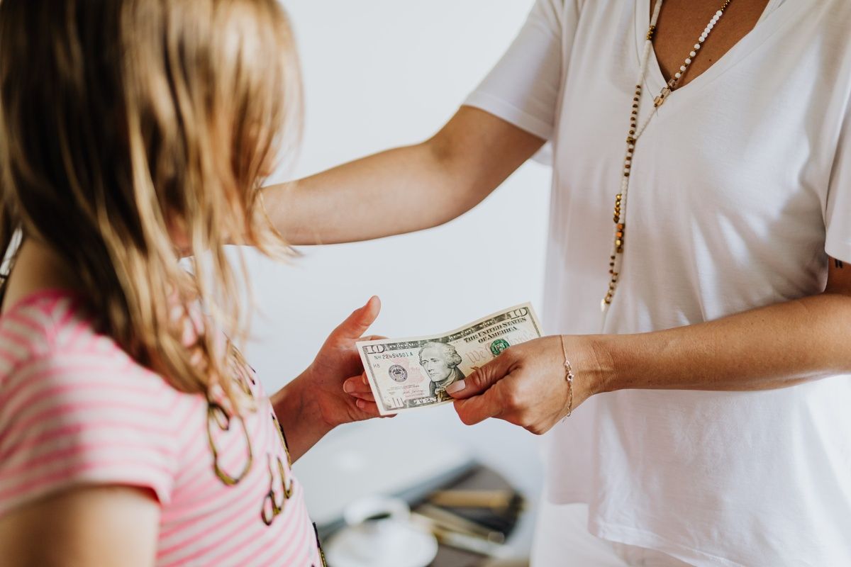 A woman is giving a girl a dollar bill.