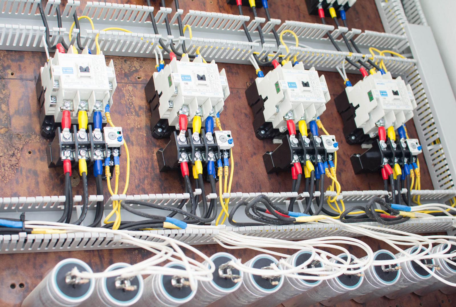 Electrical panel with colored wires connected to multiple white motor starters.