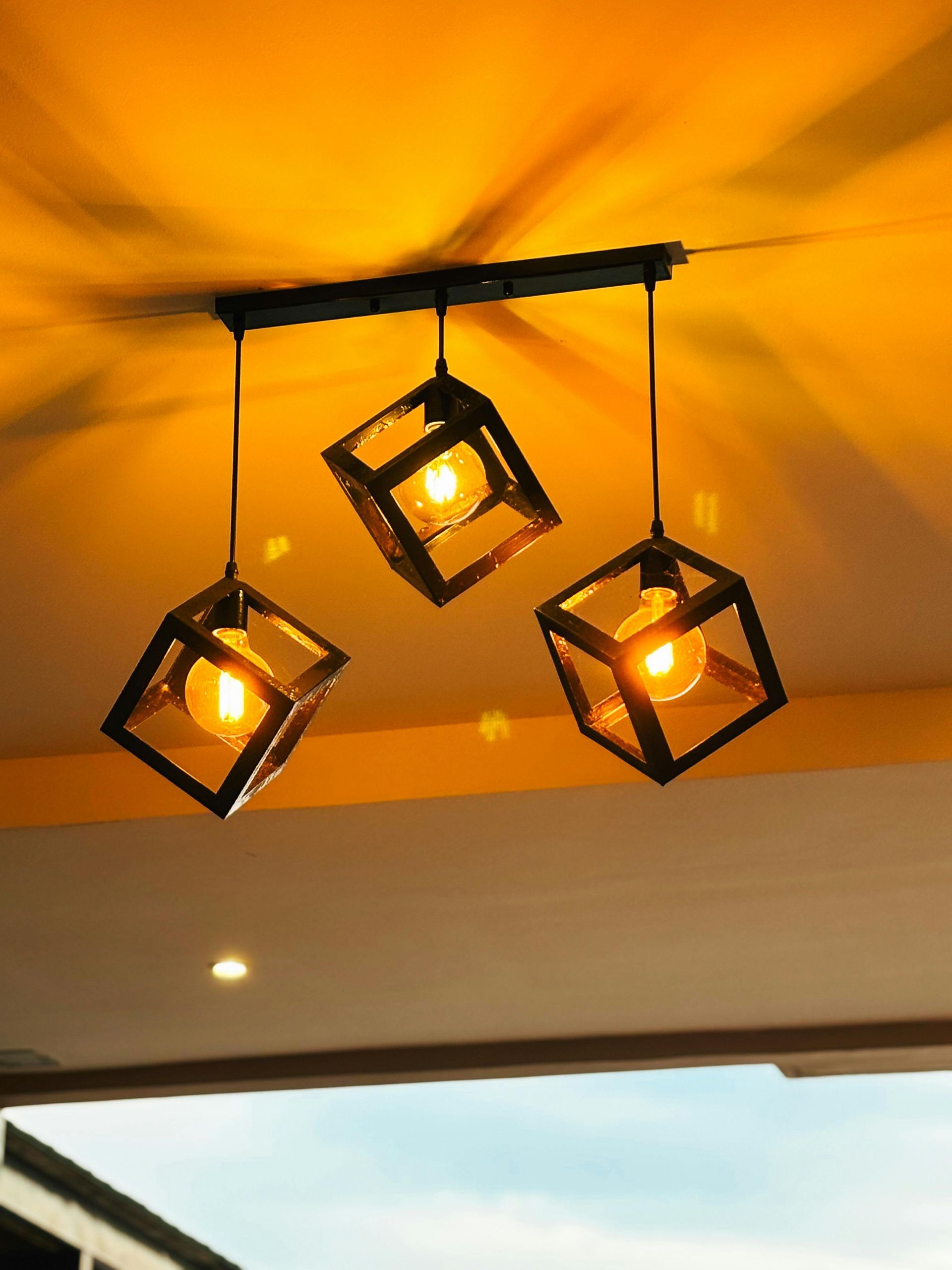 Three cube-shaped pendant lights with glowing bulbs hanging from a black bar, casting warm light.