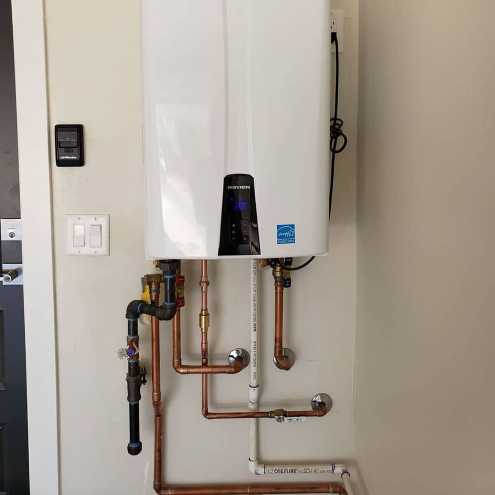 A white water heater is mounted to a wall next to copper pipes.