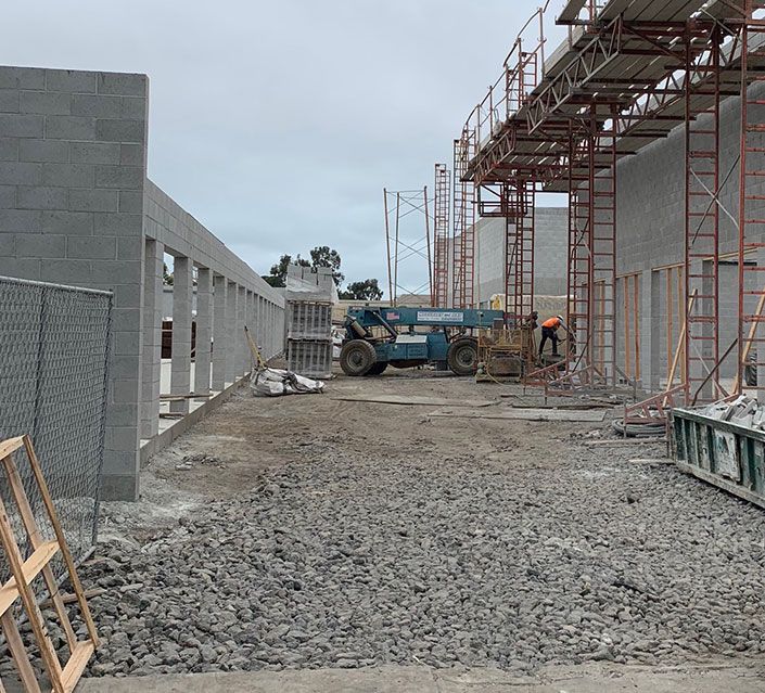 Construction site with cinder block walls, scaffolding, and a blue lift; worker in orange.