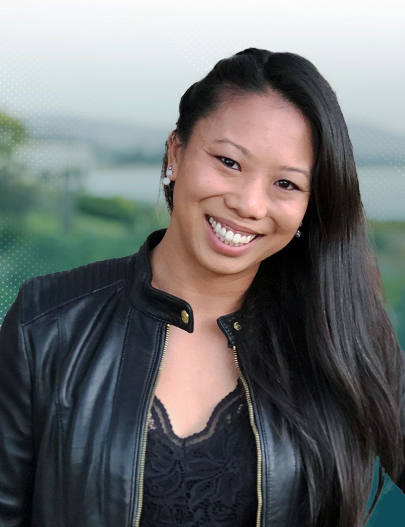 Smiling Asian woman in a black leather jacket, with a blurred outdoor background.
