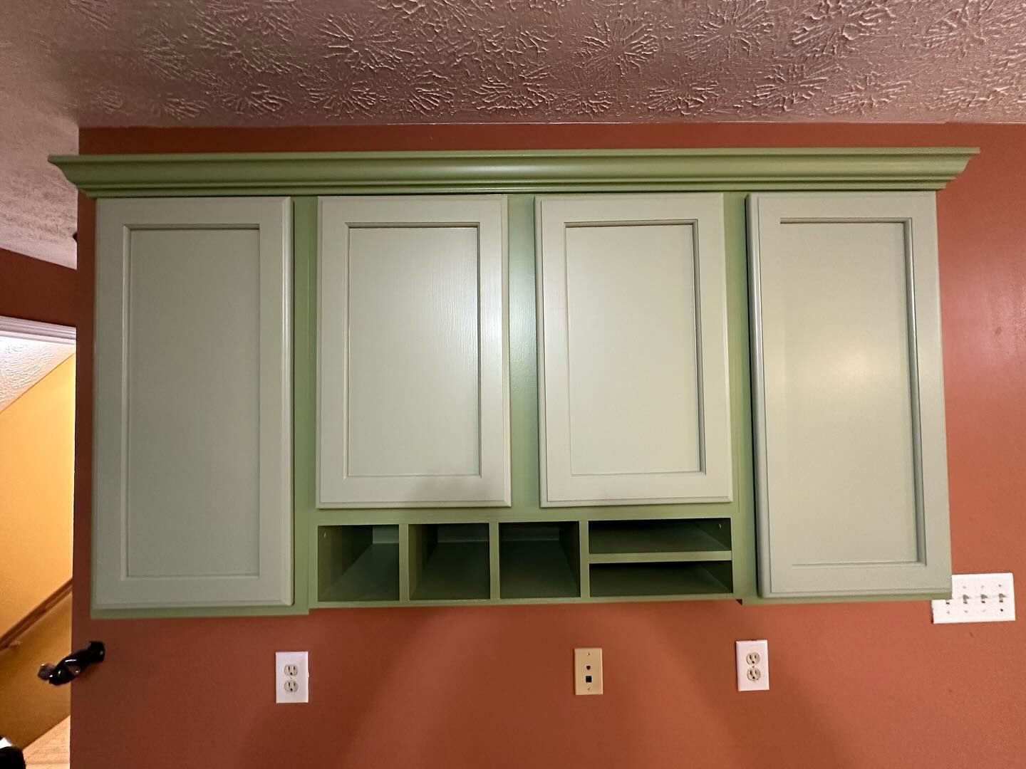 A kitchen with green cabinets and a red wall.