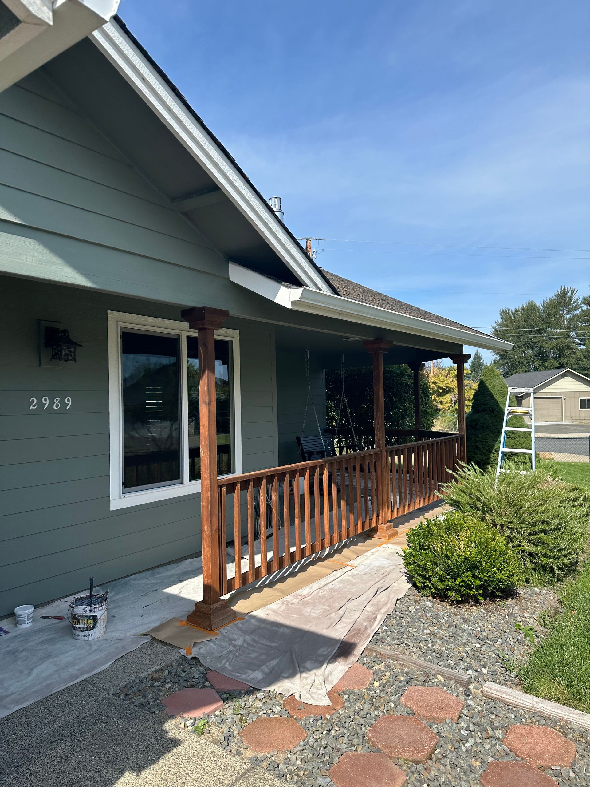 A house with a porch and a wooden railing is being painted.