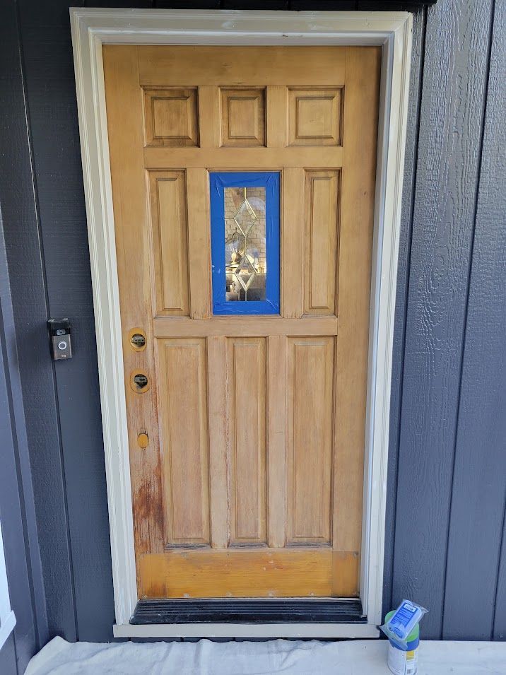 A wooden door with a blue tape on it is being painted.