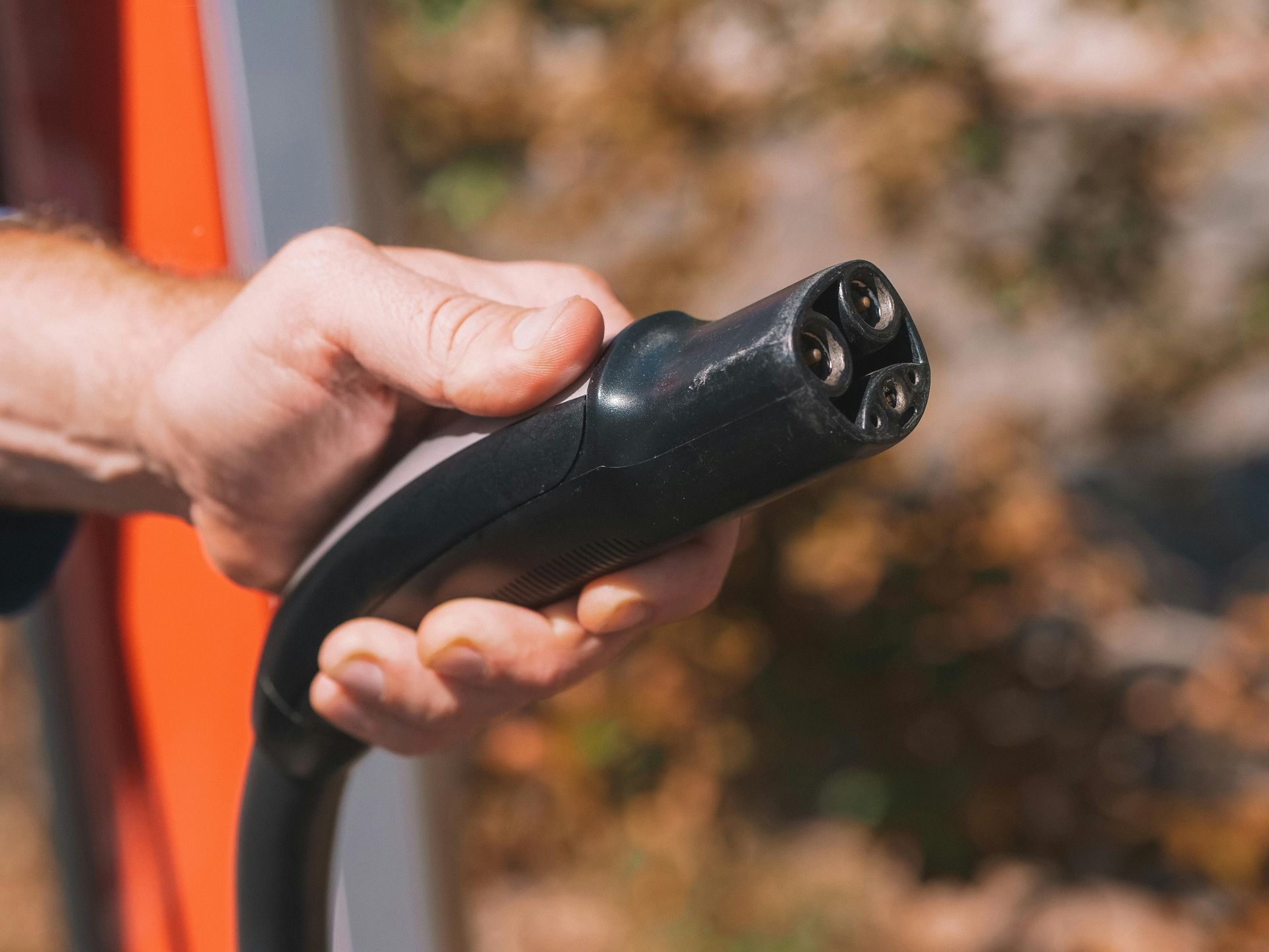 Hand holding black electric vehicle charging connector outdoors.