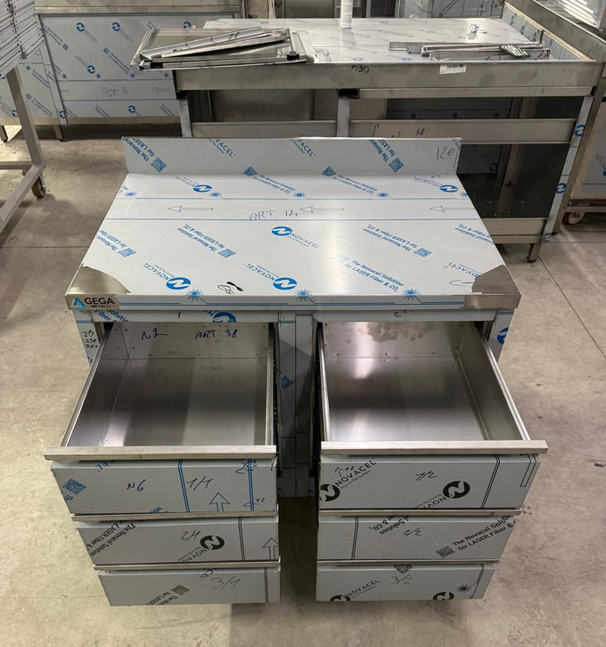 Tavolo da lavoro in acciaio inox con due cassetti a vista, in una cucina professionale, avvolto in pellicola protettiva.