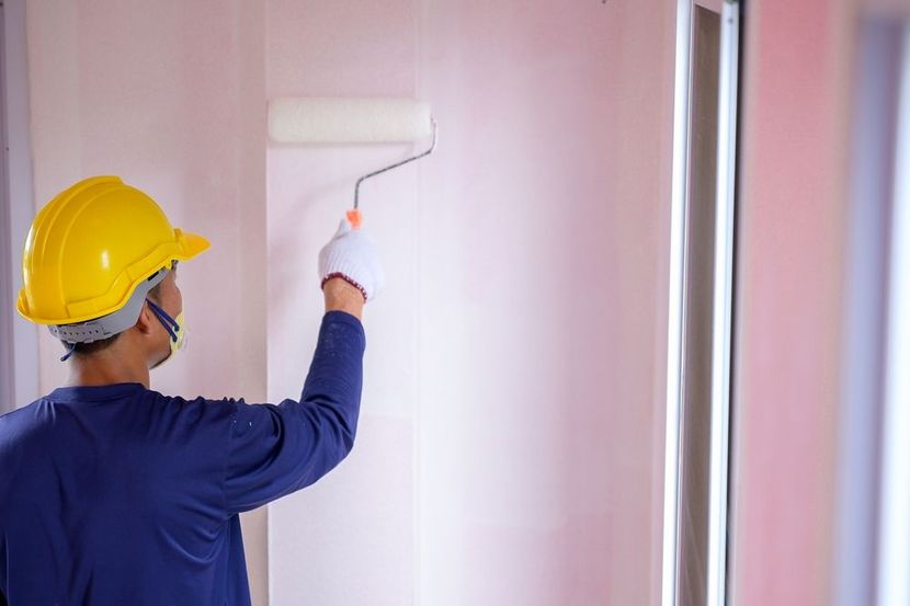 Person in yellow hard hat paints a wall with a roller.