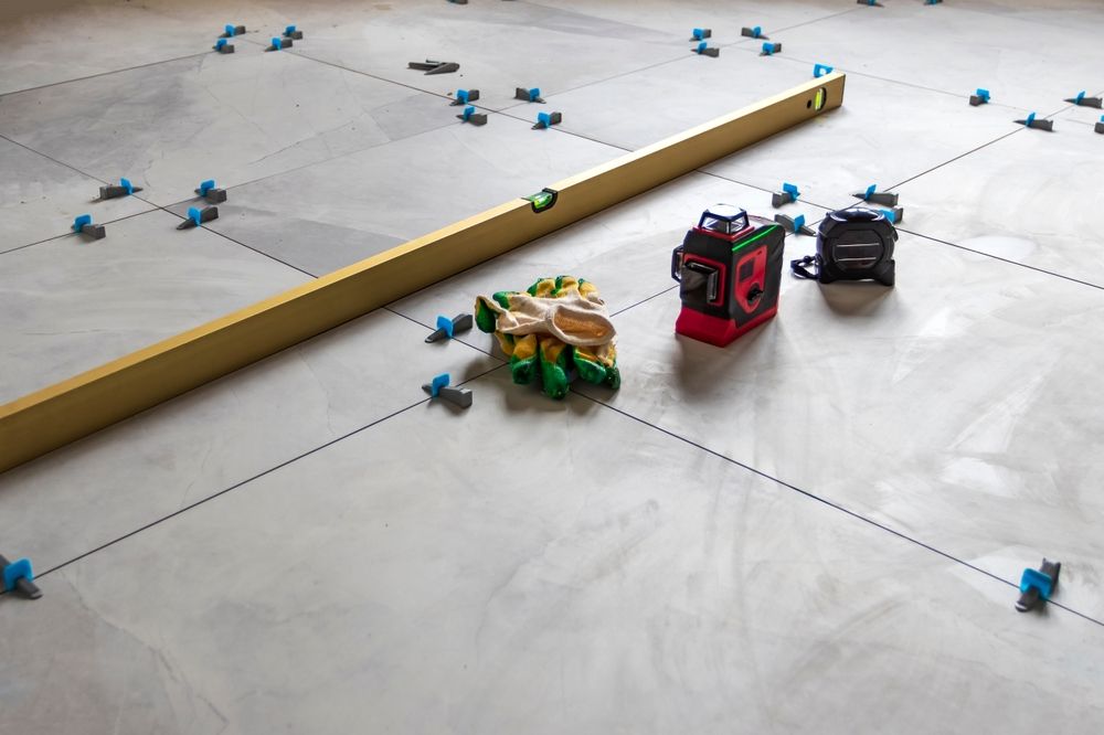 Floor tiling setup with level, tools, and spacers on concrete floor.
