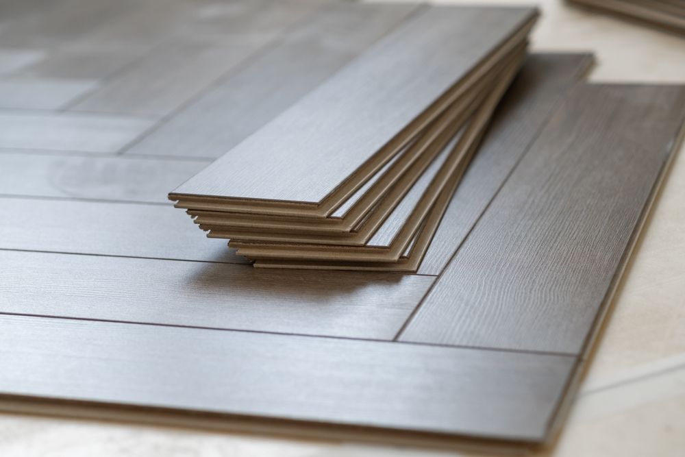 Stack of gray, wood-look flooring planks on top of installed flooring, close-up.