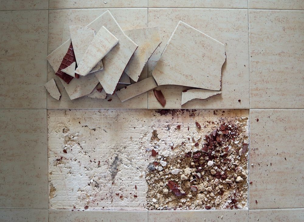 Damaged floor tiles and rubble from removal on a tan tiled floor.