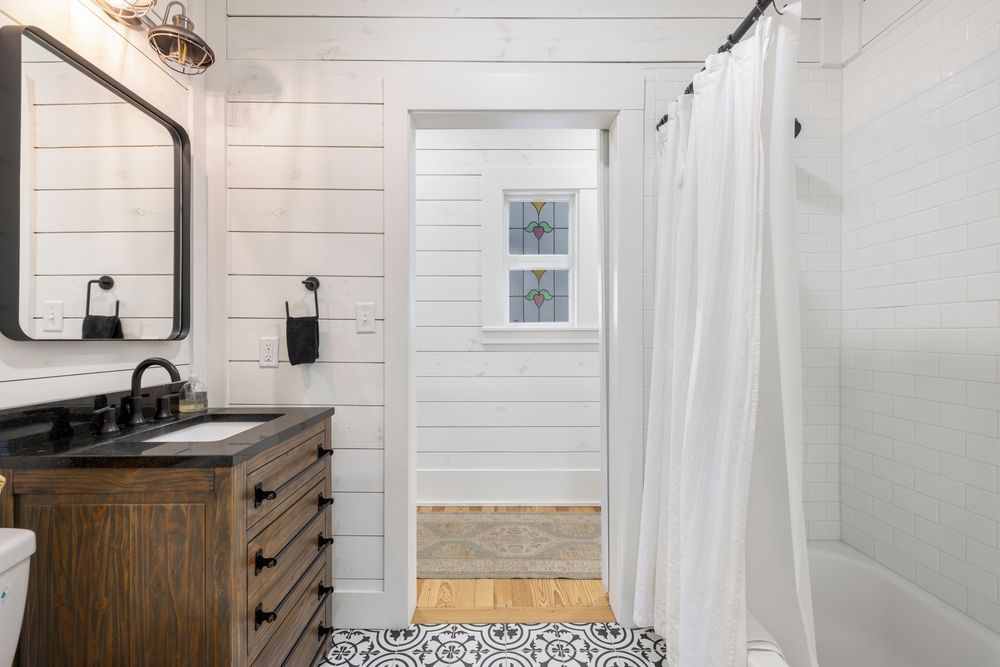 Bathroom with white plank walls, wood vanity, black fixtures, and patterned floor tile.