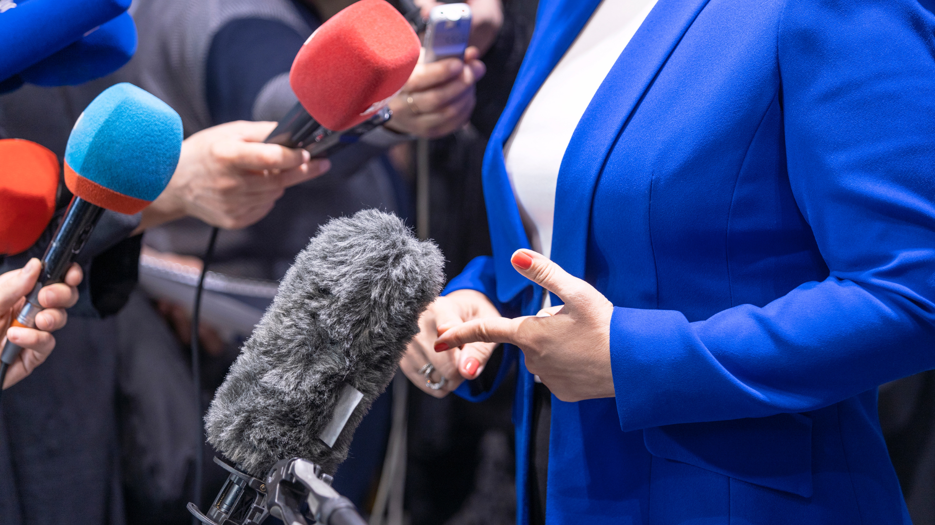 A woman in a blue jacket is talking into a microphone.