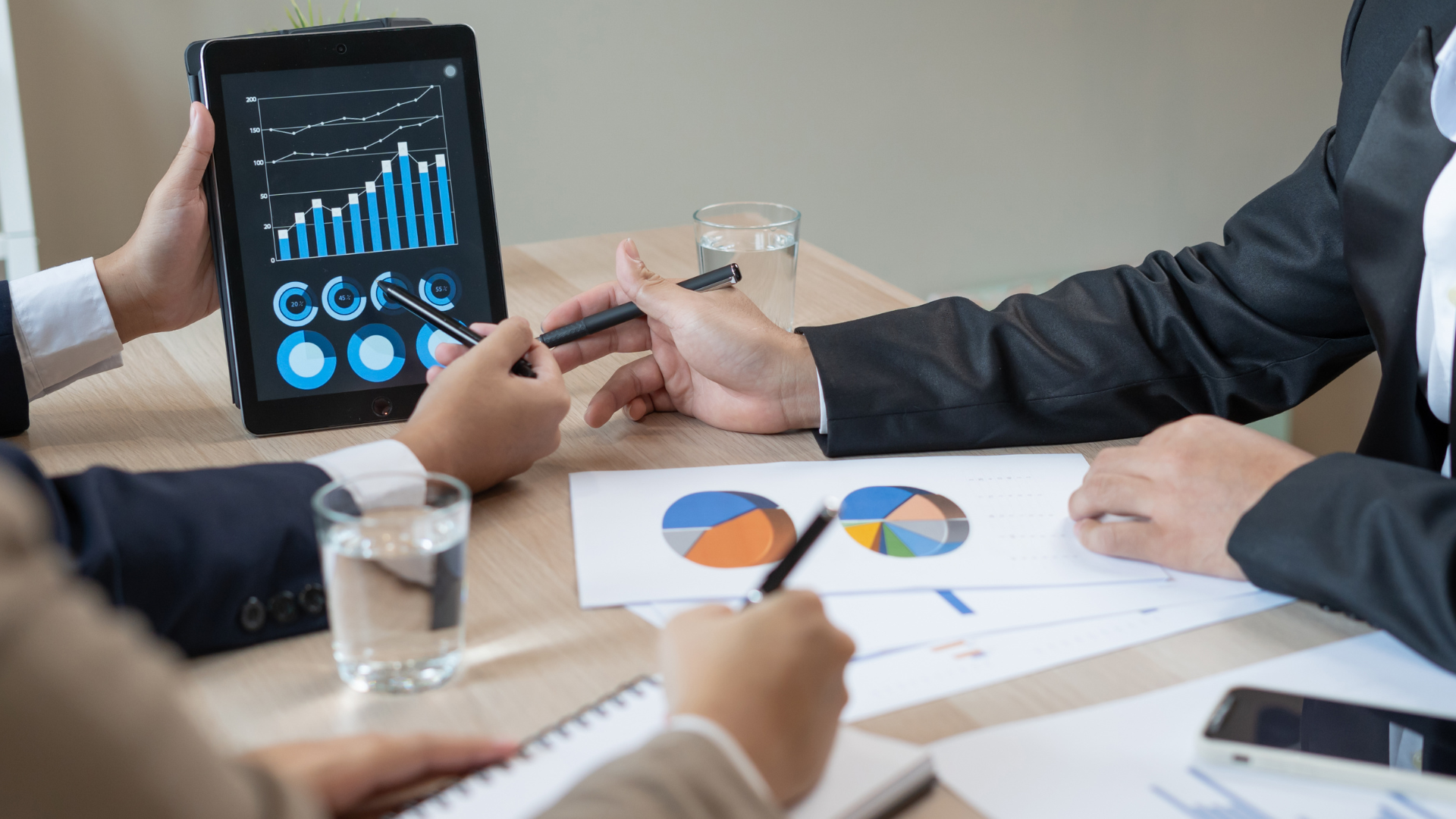 A group of people are sitting around a table looking at a tablet.