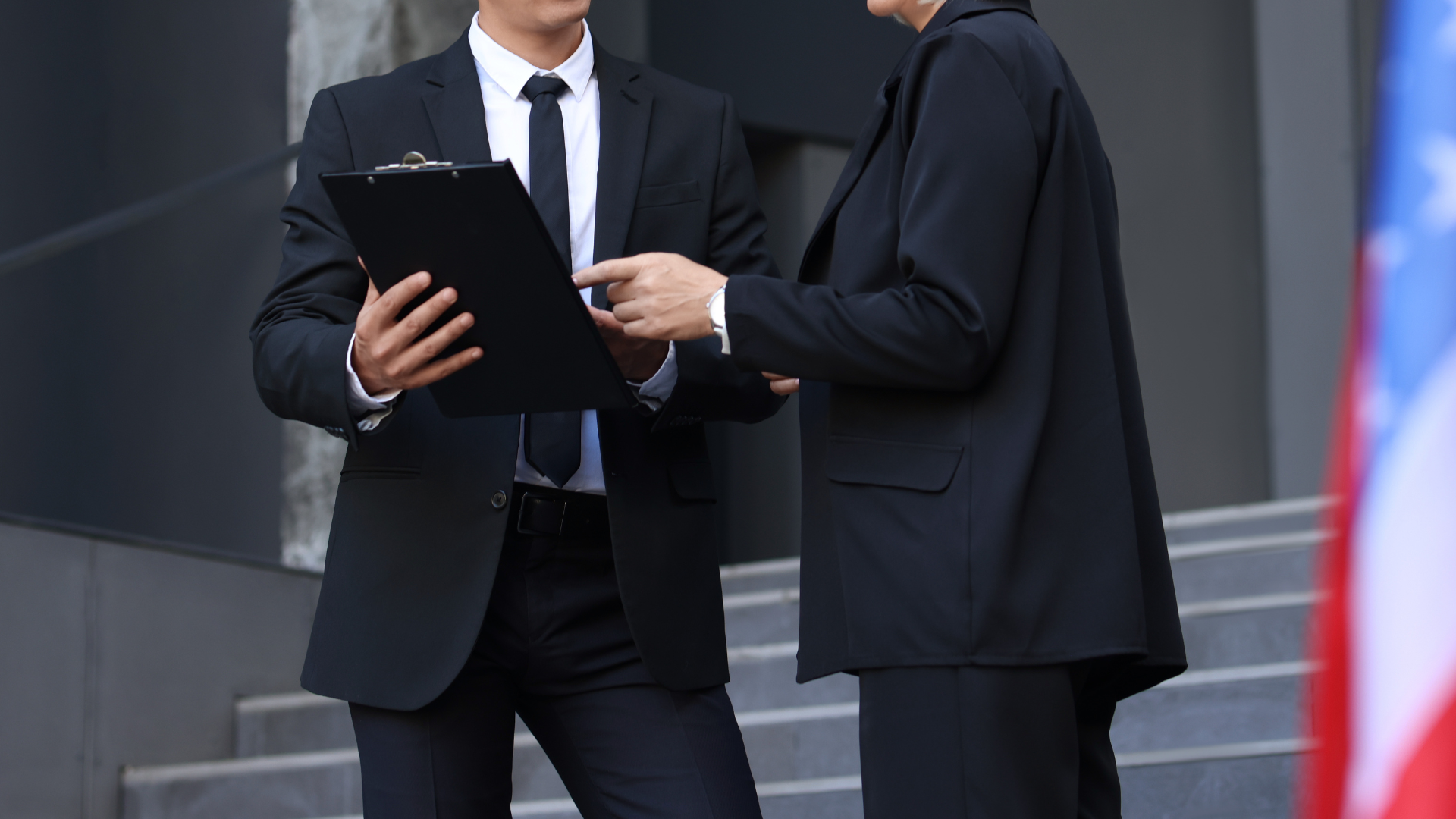 A man in a suit and tie is holding a clipboard and talking to a woman.