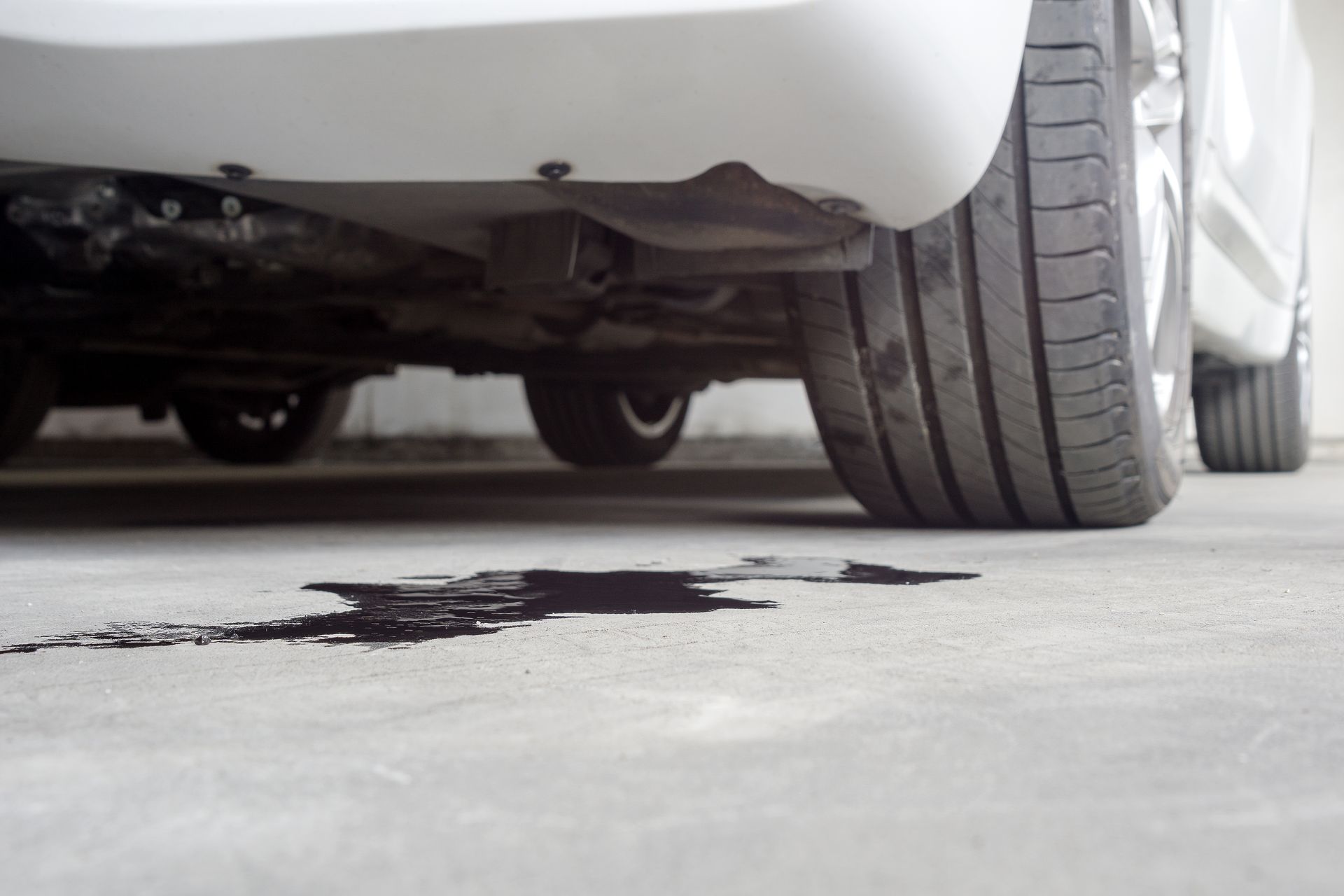 A white car is parked in a garage with a puddle of oil on the ground.