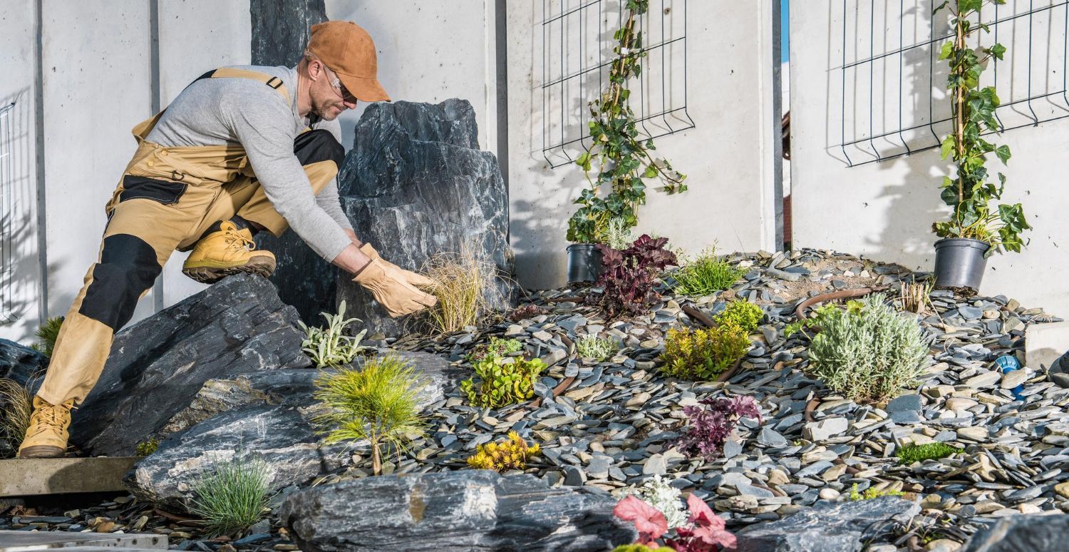 A man is working on a rock garden in front of a building.