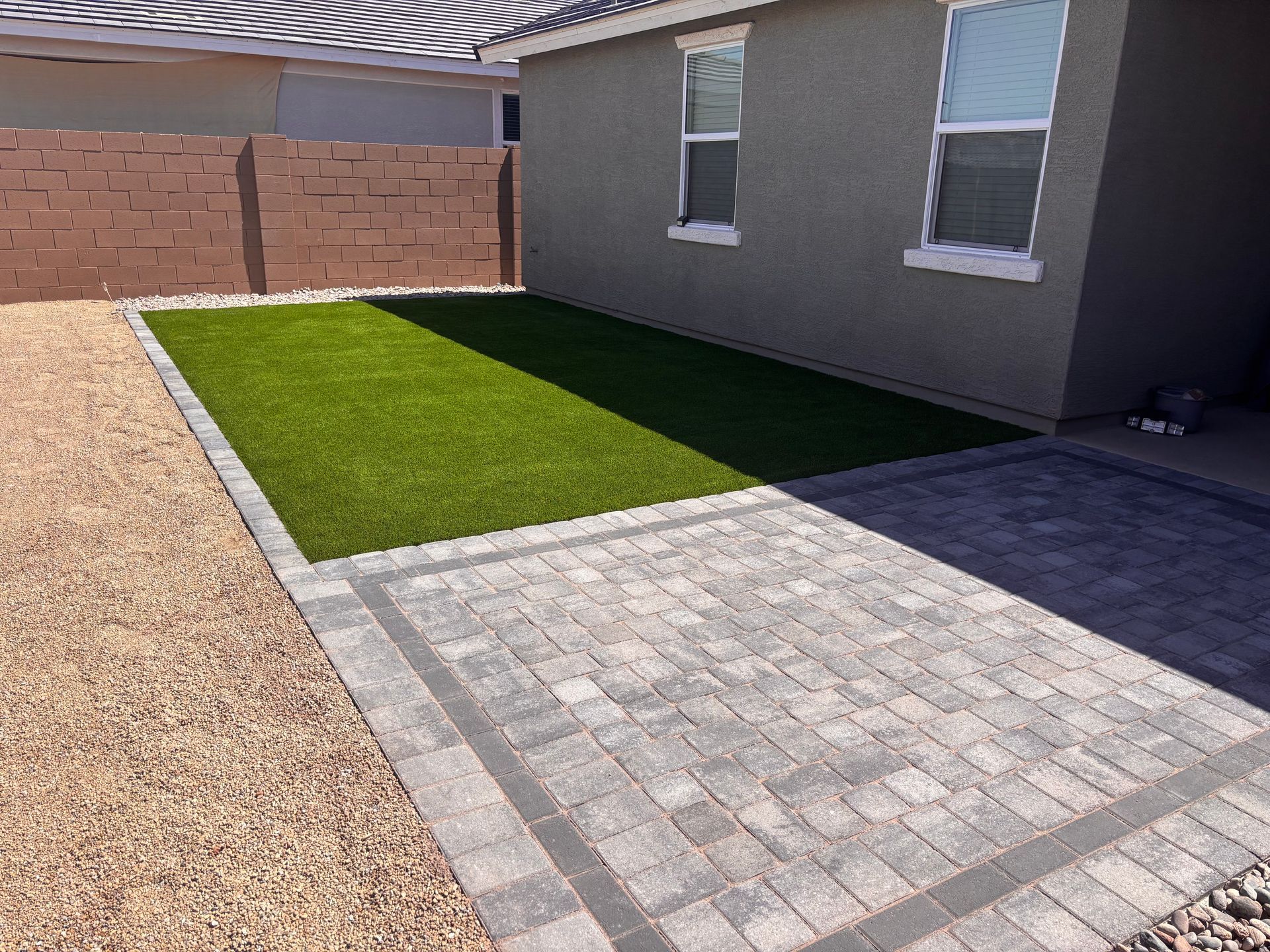 Backyard with artificial grass, paver patio, gravel, and stucco house.