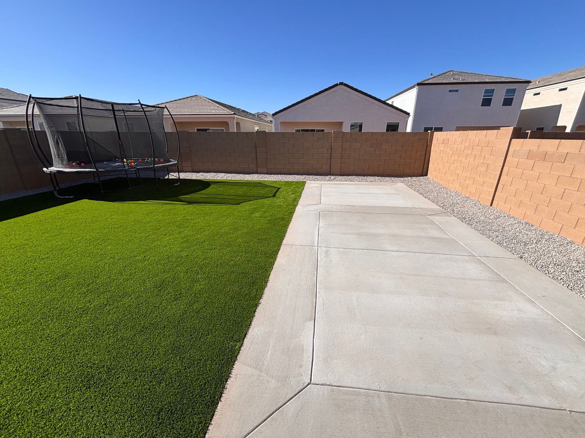 Backyard with green lawn, concrete patio, trampoline, and tan stucco walls.