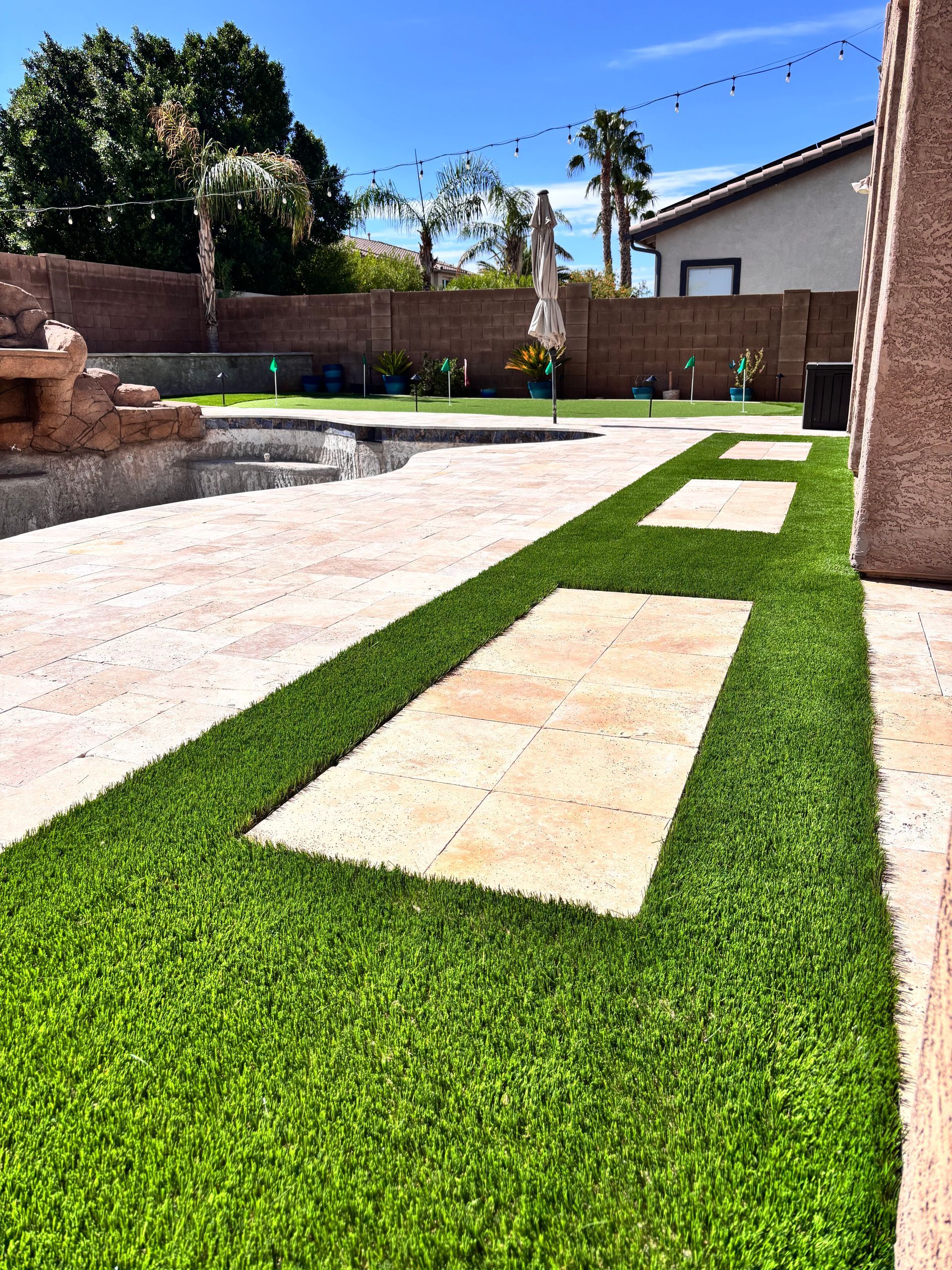 Green artificial turf with stone stepping stones in a backyard with a pool.