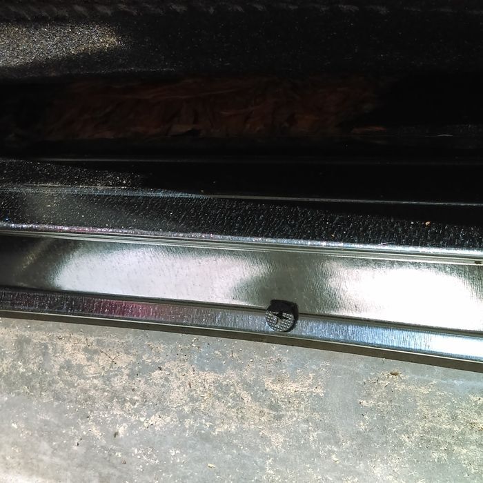 Close-up of a metal frame with a screw, reflecting light, set against a blurred background.